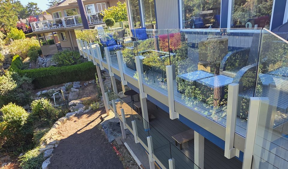 Glass railing with aluminum posts along an upper deck above a garden