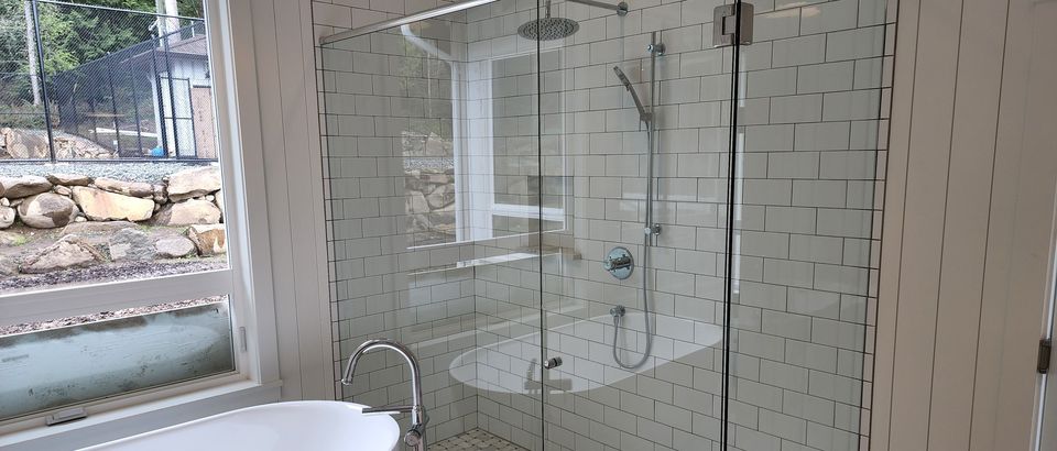 Frameless glass corner shower with subway tile beside a soaker tub